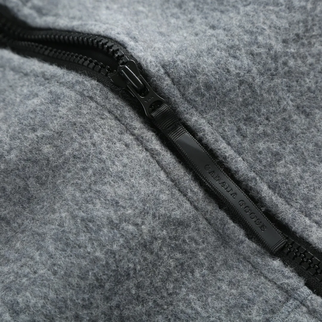 P780 Canada Goose Fleece Badge Hooded Jacket Fabric selection: Wool fleece fabric blended with wool as the main body and a very small amount of spandex and polyester fibers. Wool is a core natural ingredient that provides unparalleled temperature regulation, antibacterial and anti-odor properties and a skin-friendly feel. The feeding of a small amount of spandex gives the fabric a certain degree of four-way elasticity, making it non-restrictive during daily activities. As the basis of fleece's structure, polyester fiber enhances the fabric's durability, wrinkle resistance and quick-drying properties. It contributes to the loft of the fleece and provides functions such as trapping air.  Detail 1: The sleeves and hem are closed with 2×2 ribbing. Its strong elasticity can closely fit wrists and waists of different thicknesses, forming an effective 'seal' to prevent cold wind from blowing back. It can still maintain its original shape after repeated stretching and use, and is not easy to loose and deform. And the ribbed cuffs can convey a sense of design and enhance the visual beauty.  Detail 2: The combination of hood design and elastic buckle improves warmth and windproof performance when wearing.  Accessories: 1:1 customized elastic drawstring buckle, 1:1 customized zipper pendant, 1:1 customized armband SIZE: S M L XL